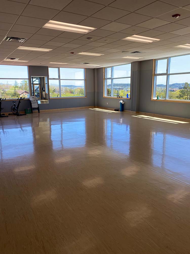 A wide angle of a fairly empty fitness room with large windows
