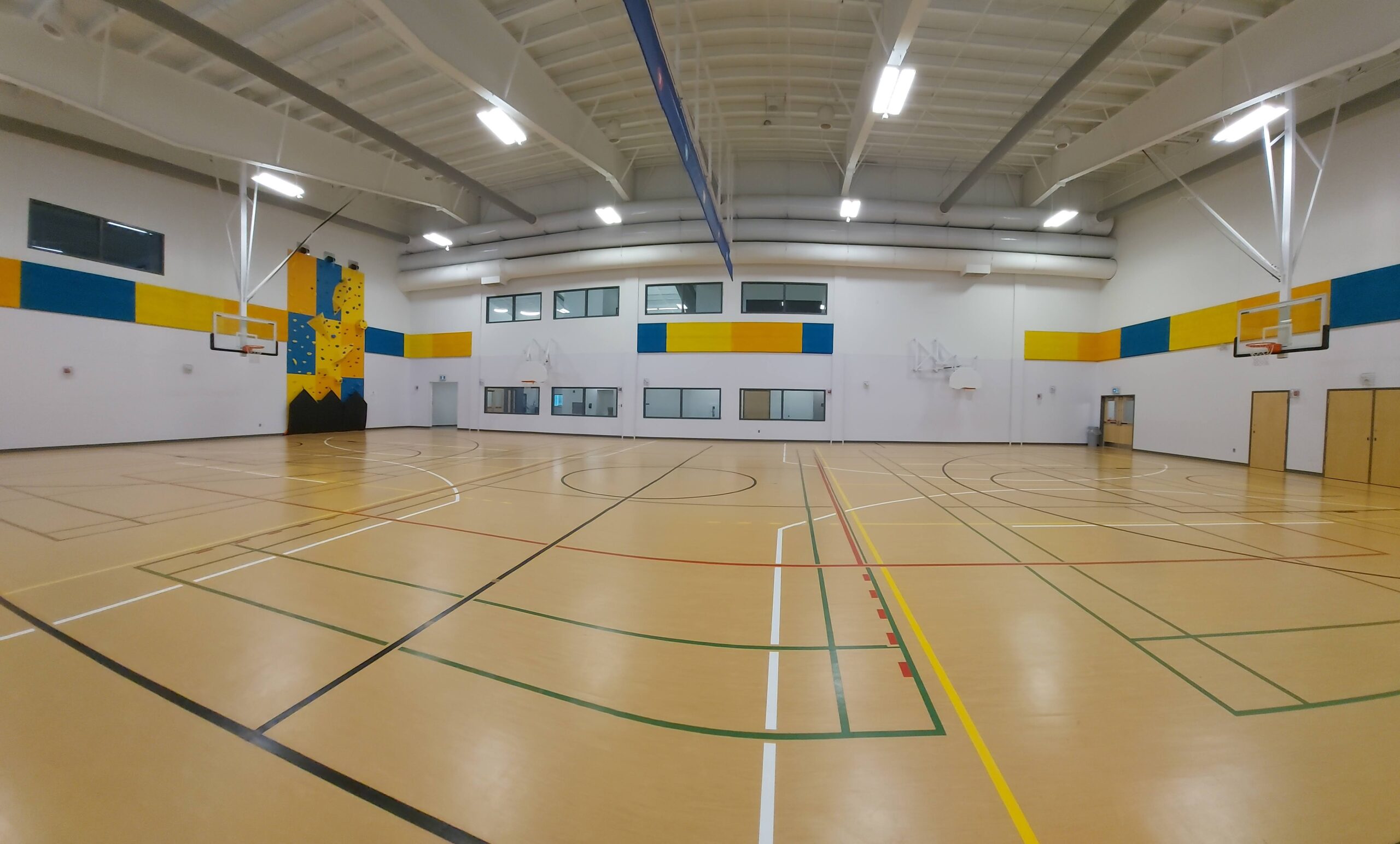 a wide angle view of a gymnasium with basketball nets and a rock climbing wall