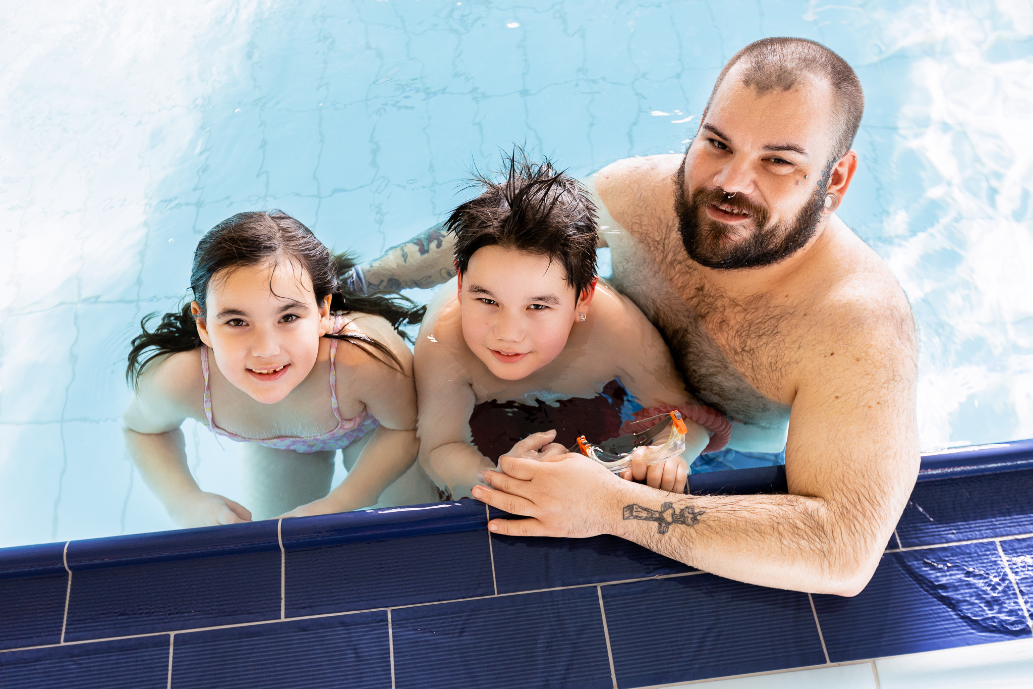 two children and a man smile for a photo in a pool