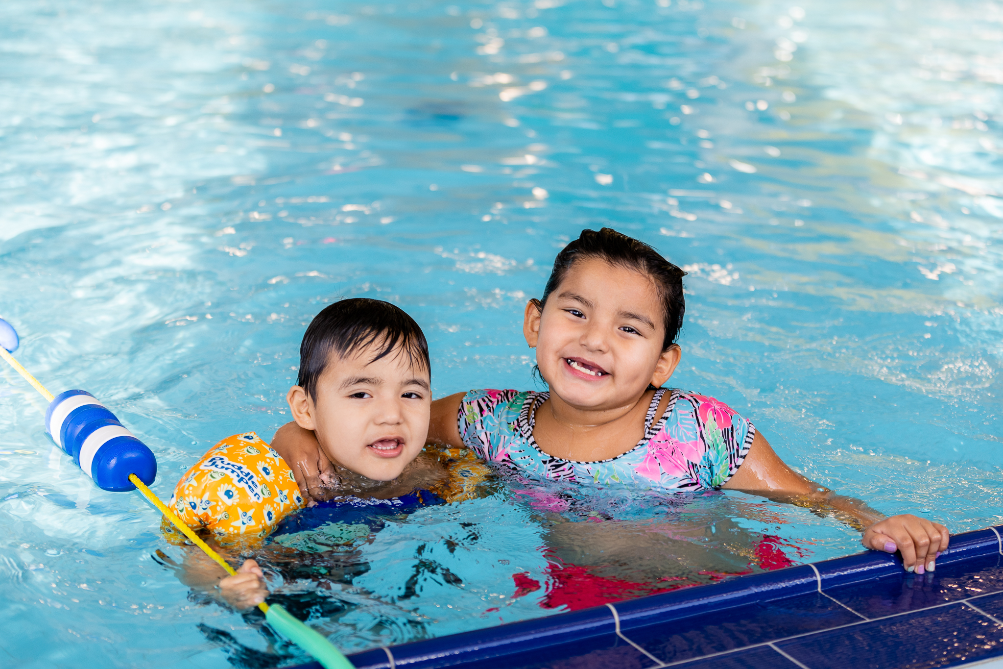 two children swimming in a pool smile for a photo