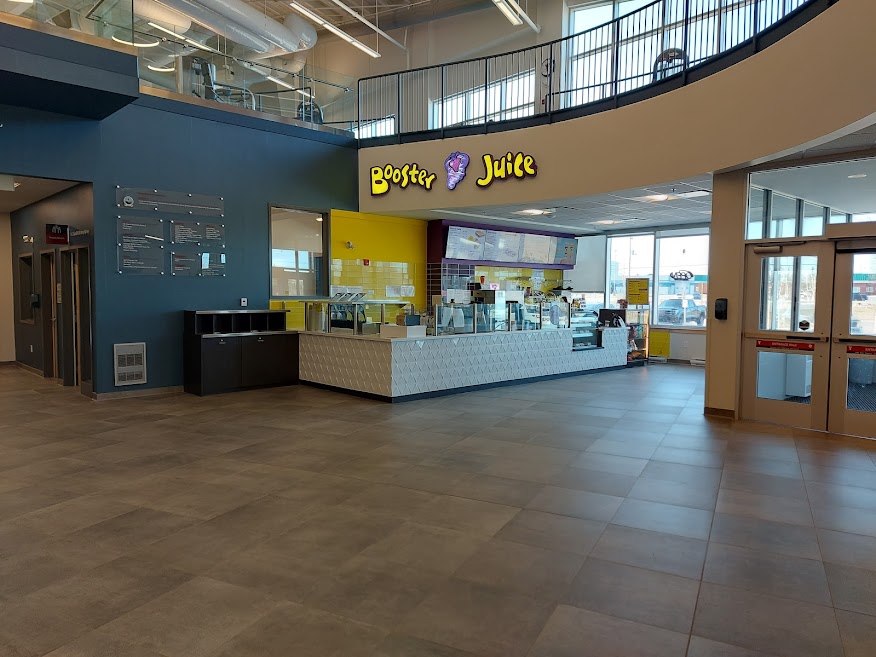 A Booster Juice booth is shown from a far in the lobby of a YMCA.