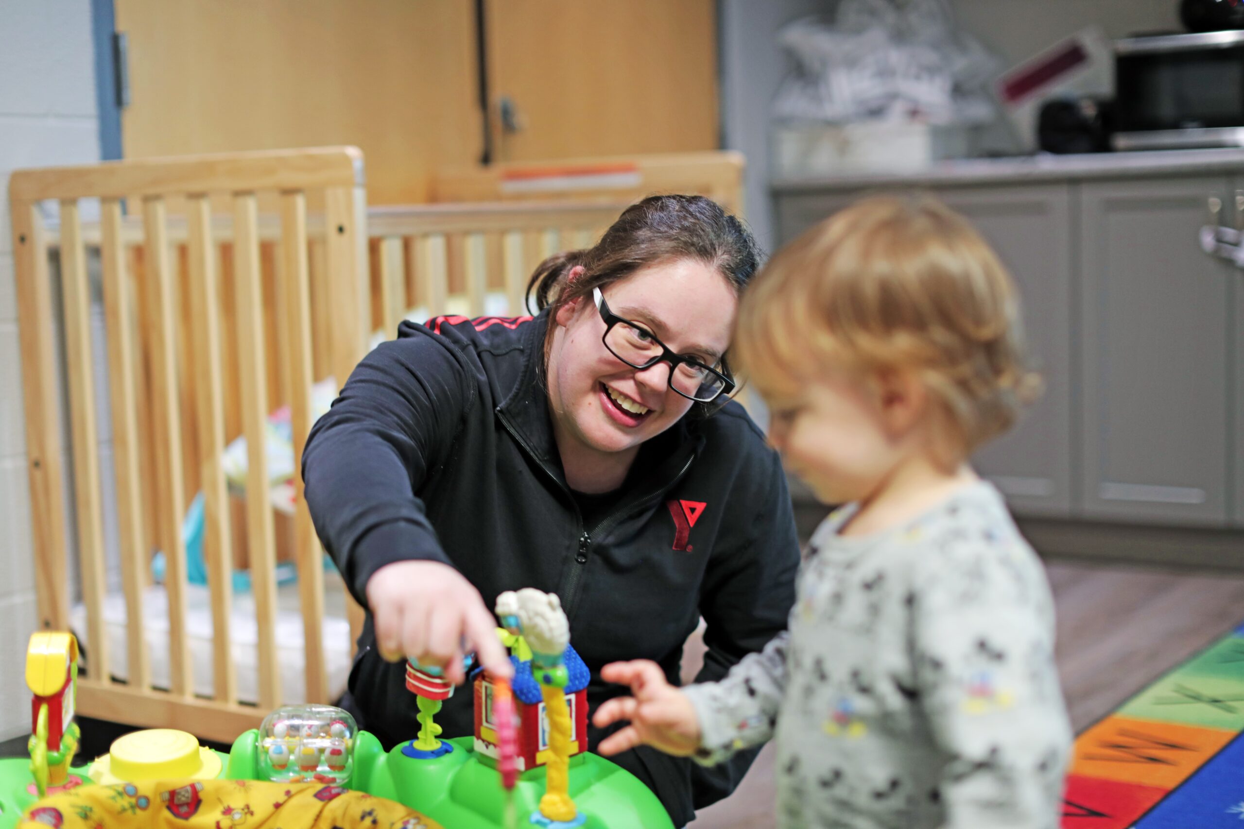 A YMCA employee smiling and playing with toys with a child
